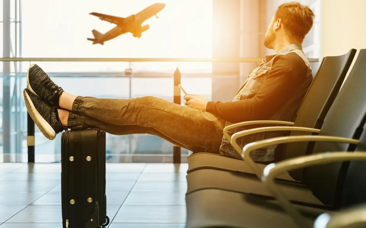 International traveler waiting at an airport with luggage while checking flight updates