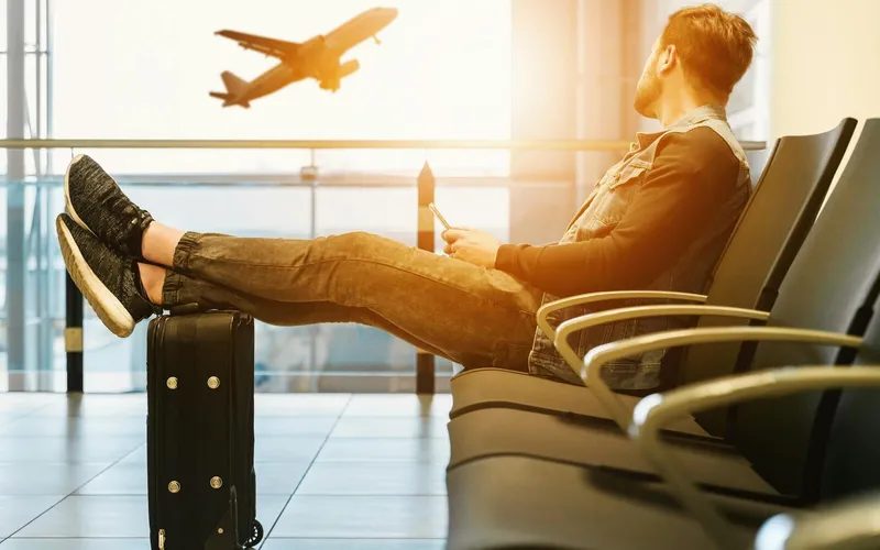 International traveler waiting at an airport with luggage while checking flight updates