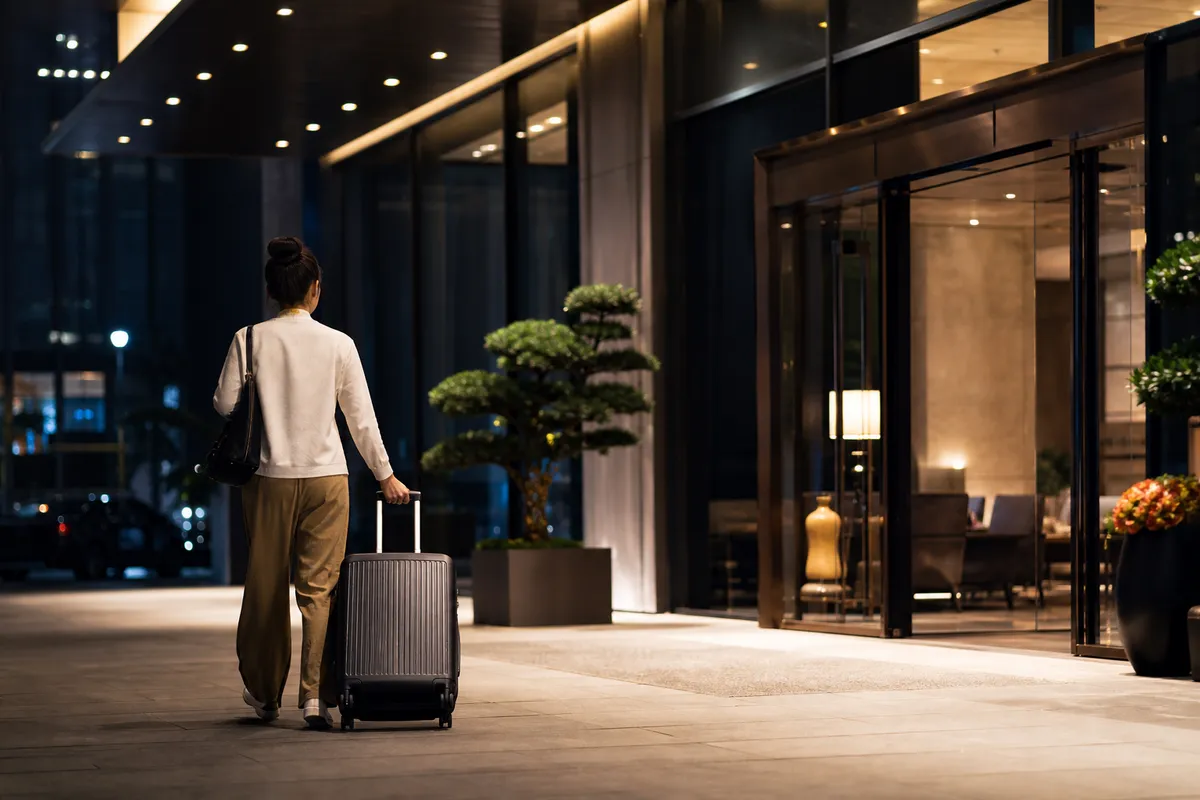 Traveler arriving late at night outside a modern hotel entrance in China with luggage