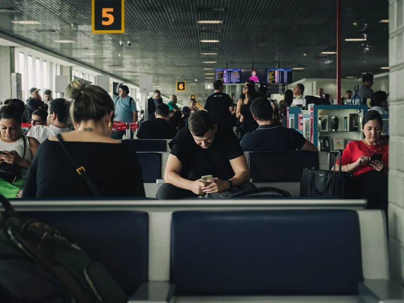 Travelers checking phones while waiting at an airport before a flight