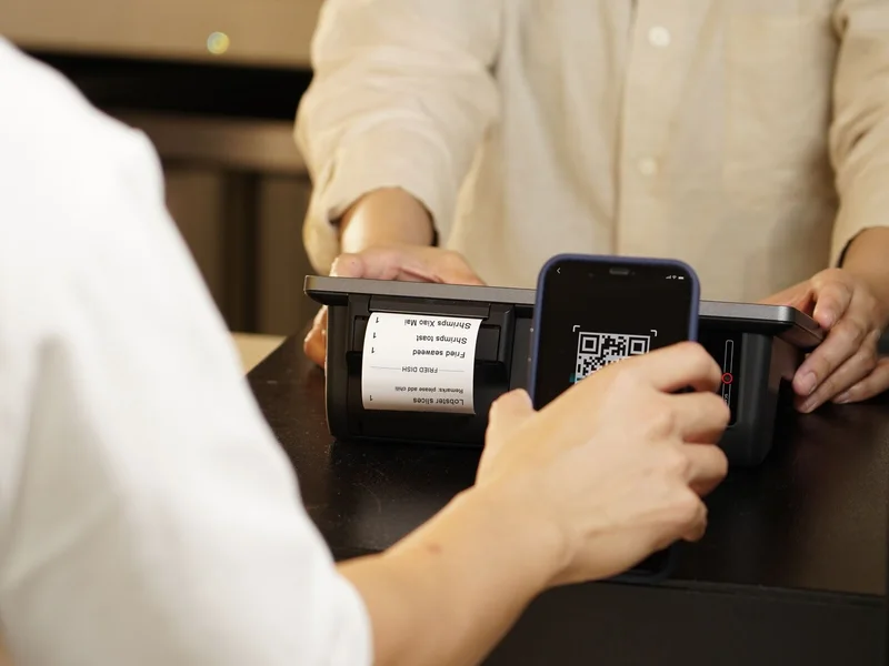 Customer presenting a phone QR code at a payment counter during a cashless transaction