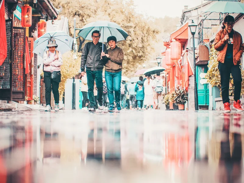 People walking with umbrellas on a rainy street in Beijing during a sightseeing day