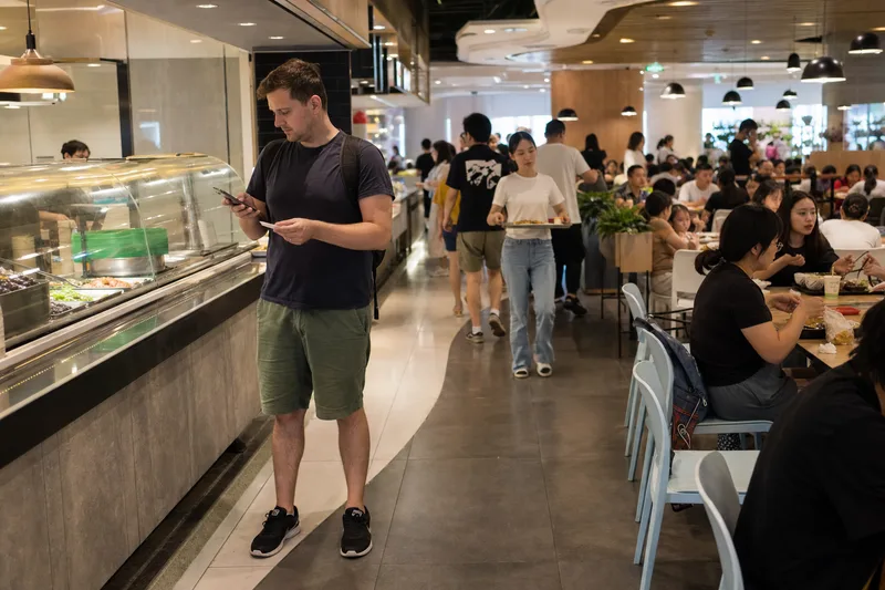 Traveler checking an order beside a food counter in a Chinese food court